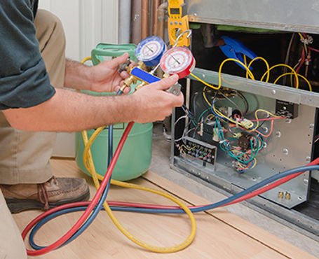 A technician from West Coast Refrigeration using manifold pressure gauges and a refrigerant tank to service an HVAC and refrigeration system.